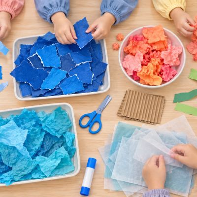 材料排成海洋色：從正上方看孩子整理藍色紙、瓦楞紙、薄色紙和安全工具。